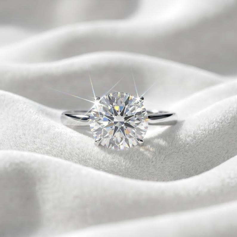 May include: A silver-toned ring featuring a large, round, brilliant-cut clear gemstone set in a four-prong setting. The gemstone exhibits multiple facets that catch the light, creating a starburst effect with bright white reflections.