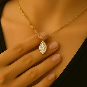 May include: A gold chain necklace with a marquise-shaped pendant set with clear stones.