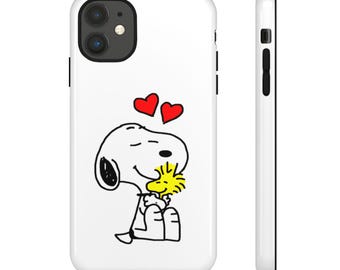 May include: A white smartphone case featuring a black line drawing of Snoopy hugging Woodstock. Two red hearts are positioned above the characters. The case has a black camera cutout and black side buttons, shown from both the back and side views.