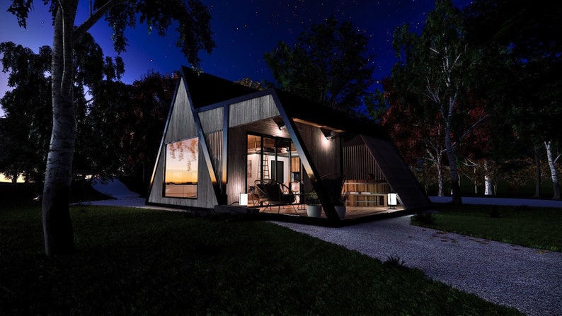 Pode incluir: Uma cabana moderna de forma triangular com uma grande janela, revestimento de madeira e uma moldura de metal preto. A cabana est&aacute; iluminada &agrave; noite e cercada por &aacute;rvores.