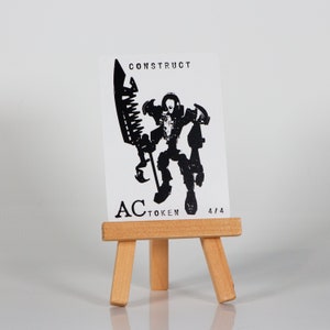May include: A black and white illustration of a robot holding a large weapon. The image is printed on a white card with the text "CONSTRUCT AC TOKEN 4/4".