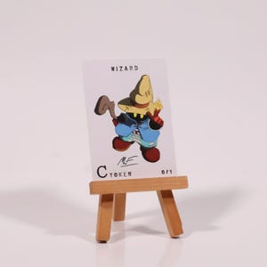 May include: A white card with the word "WIZARD" at the top, featuring a cartoon wizard character in a hat, blue pants, and red shoes. The card is displayed on a small wooden easel. The text "C TOKEN" and "0/1" are also visible.