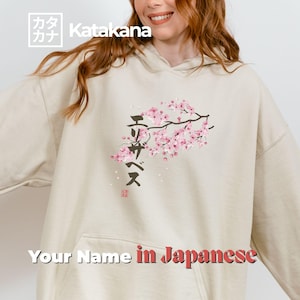 Puede incluir: Sudadera con capucha beige con un diseño de rama floral en rosa y negro. La sudadera con capucha presenta texto japonés y la frase "Your Name in Japanese" en rojo y blanco. La esquina superior izquierda tiene el texto "Katakana".
