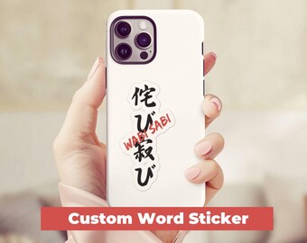 May include: White phone case with a black and red custom word sticker that says "Wabi Sabi" and Japanese characters.