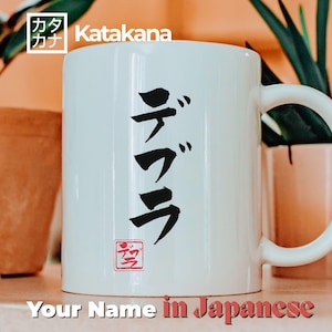 Op de afbeelding: Witte keramische mok met een zwart Japans Katakana-karakterontwerp. De mok heeft een gebogen handvat en een rood stempelachtig symbool aan de onderkant. De tekst "Your Name in Japanese" staat onderaan de afbeelding.