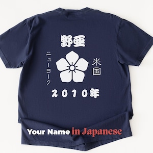 Może przedstawiać: Granatowa koszulka z białymi japońskimi znakami i kwiatowym wzorem. Tekst zawiera "2010" i "Your Name in Japanese". Codzienna odzież.