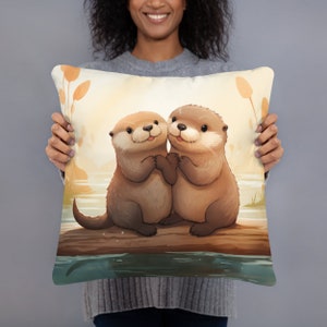 May include: A decorative throw pillow featuring a cartoon illustration of two otters hugging on a log in a lake. The otters are brown and have big eyes and smiles. The background is a soft yellow with green reeds.