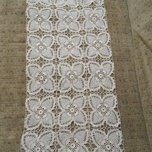 Puede incluir: Un camino de mesa blanco de ganchillo con un patrón cuadrado de intrincados diseños florales.