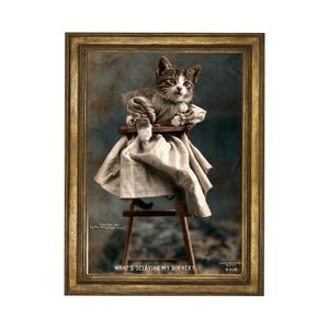 Puede incluir: Una impresión enmarcada de estilo vintage que muestra a un gatito atigrado con una prenda beige con volantes, sentado en una trona de madera. El texto "WHAT'S DELAYING MY DINNER?" aparece en la parte inferior, junto a "Copyright 1903" y "B 838".
