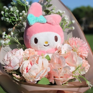 Könnte beinhalten: Ein rosa Plüschtier mit Hasenohren und einer blauen Schleife ist von einem Strauß rosa und weißer Blumen in braunem Papier umhüllt.