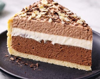 May include: A slice of layered chocolate cake on a black plate. The cake features a dark chocolate base, a white cream layer, and a lighter chocolate mousse topping, garnished with chocolate shavings and almond slivers.