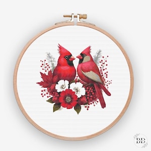 Op de afbeelding: Borduurpatroon met twee rode kardinaals, die op een tak zitten met rode bessen en witte bloemen. De kardinaals kijken elkaar aan en lijken te zingen.
