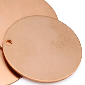 May include: Close-up of three copper-colored metal discs. Each disc is round with a small hole near the edge. The discs are overlapping, showcasing their smooth, reflective surfaces. Ideal for jewelry making or crafting.
