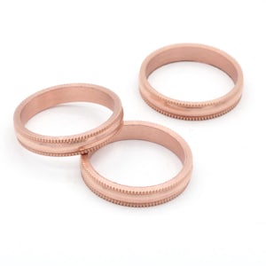 May include: Three rose gold rings with a textured, dotted design around the center. The rings are displayed on a white background. These rings are suitable for weddings or everyday wear.
