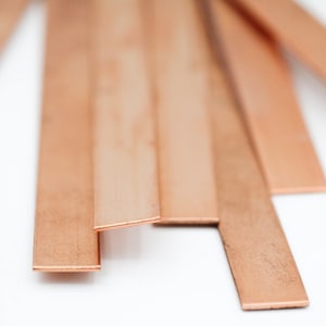May include: A stack of thin, flat copper strips, arranged in a staggered pattern. The strips are a warm, reddish-brown color and have a slightly textured surface.