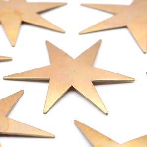 May include: Several bronze-colored, seven-pointed star ornaments are scattered on a white background. The stars have a metallic sheen and are arranged in a seemingly random pattern, with varying orientations.