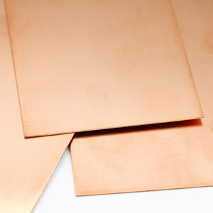 May include: Three sheets of thin, copper-colored metal stacked on top of each other. The sheets are smooth and have a slightly reddish hue.