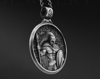 May include: Silver pendant necklace featuring a detailed, three-dimensional design of a warrior holding a spear and shield. The pendant is round and hangs from a silver chain.