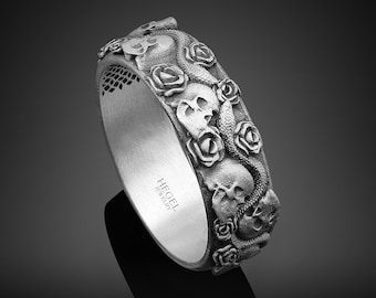 Könnte beinhalten: Ein silberner Ring mit einem detaillierten Design aus Totenköpfen und Rosen. Der Ring ist mit den Worten "HEGEL JEWELRY" graviert.