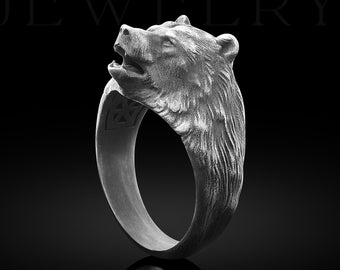 May include: A silver ring with a bear head design. The bear's head is facing to the right and has a detailed, textured finish.