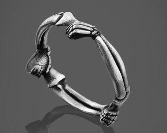 May include: A silver ring shaped like two hands clasped together, with detailed bone-like features.