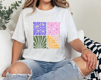 May include: A light gray t-shirt with a graphic design of four colorful squares featuring stylized flowers. The squares are arranged in a 2x2 grid.