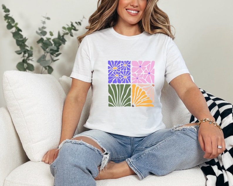 May include: A white t-shirt with a graphic design of four colorful squares featuring stylized flowers. The squares are arranged in a 2x2 grid.