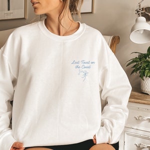 May include: White sweatshirt with a blue embroidered design that says "Last Toast on the Coast" with two wine glasses and a bow.