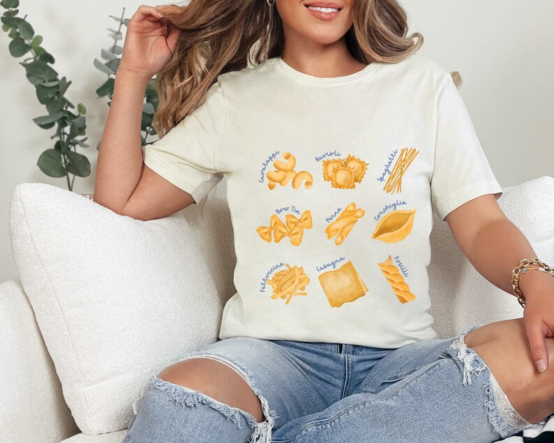 May include: A white t-shirt with a graphic of different types of pasta, including spaghetti, tortellini, and lasagna. Each pasta type is labeled with its Italian name.