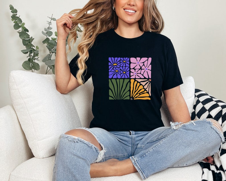 May include: A black t-shirt with a graphic design of four squares featuring different floral patterns in shades of purple, pink, green, and yellow.