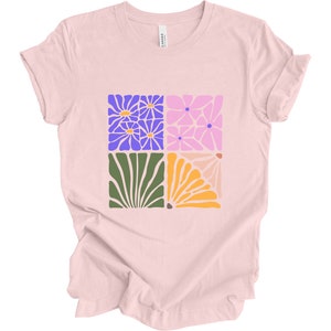 May include: A pink t-shirt with a graphic design of four squares featuring stylized floral patterns in shades of purple, pink, green, and orange.