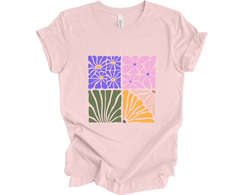 May include: A pink t-shirt with a graphic design of four squares featuring stylized floral patterns in shades of purple, pink, green, and orange.