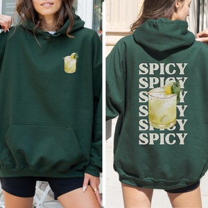 May include: A dark green hoodie with a pocket on the front and a graphic of a margarita on the front. The back of the hoodie has the word "Spicy" repeated five times in a light beige color.