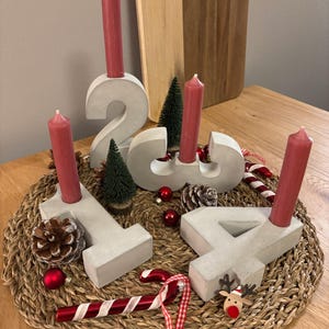 Graue Adventszahlen als Set von 1-4 aus Beton mit Kerzen in der Farbe altrosa, dekoriert mit Tannenzapfen, Kugeln, Zuckerstangen, auf geflochtenem Untersetzer