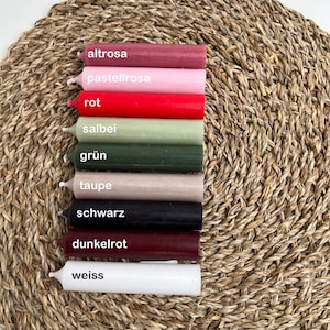 Neun Stabkerzen in den Farben altrosa, pastellrosa, rot, salbei, grün, taupe, schwarz, dunkelrot und weiß auf Untersetzer