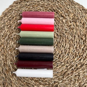Neun Stabkerzen in den Farben altrosa, pastellrosa, rot, salbei, grün, taupe, schwarz, dunkelrot und weiß auf Untersetzer
