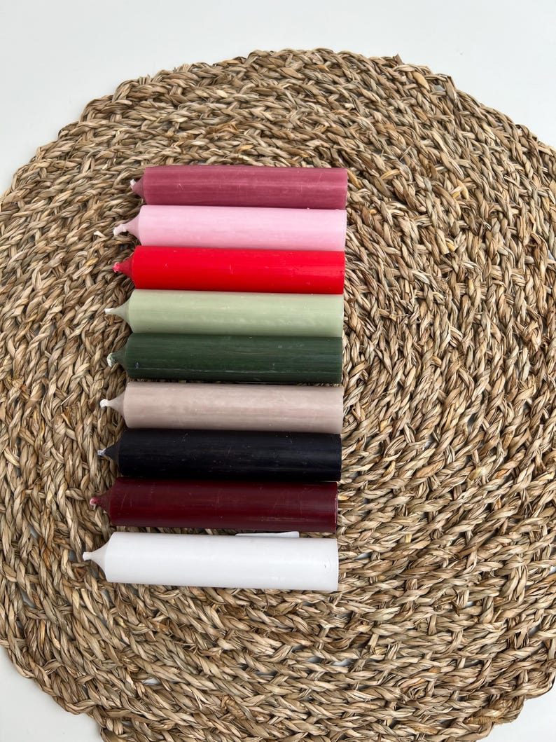Neun Stabkerzen in den Farben altrosa, pastellrosa, rot, salbei, grün, taupe, schwarz, dunkelrot und weiß auf Untersetzer