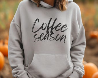 Puede incluir: Una sudadera gris con capucha con un gráfico negro que dice "Coffee Season" en una fuente manuscrita. La sudadera tiene un bolsillo canguro.