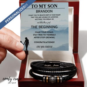 Puede incluir: Un brazalete de cuero negro con un cierre plateado y un mensaje que dice "love you forever". El brazalete está en una caja de madera con una tarjeta que dice "To My Son Brandon" y un mensaje de aliento.