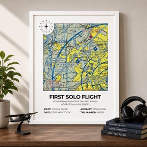 May include: A framed aviation map print titled FIRST SOLO FLIGHT featuring Morristown Municipal Airport, New Jersey. The text includes pilot John R. Smith, date February 7, 2026, aircraft Cessna 172N, and tail number N6565J. The map displays yellow and blue aeronautical charts.