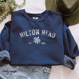 May include: A navy blue sweatshirt with a white graphic of a sea turtle and the text "HILTON HEAD EST. 1963".