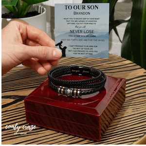 Puede incluir: Un brazalete de cuero negro con un dije de plata y una pequeña caja. La caja tiene una tapa roja y un mensaje en el interior que dice "A nuestro hijo Brandon, quiero que creas en lo profundo de tu corazón que eres capaz de lograr todo lo que te propongas. Nunca pierdas. O ganas o aprendes. Solo avanza y apunta a las estrellas. No puedo prometer estar aquí por el resto de tu vida, pero puedo prometer amarte por el resto de la mía. Te amo para siempre."