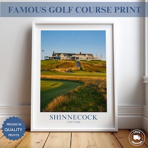 May include: A framed wall art print featuring a landscape photograph of the Shinnecock golf course in New York. The image displays a large clubhouse atop a grassy hill overlooking a green fairway with golden-hued tall grass under a clear blue sky.
