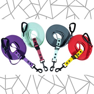 May include: Four retractable dog leads in different colours: purple, mint green, grey, and red. Each lead has a black clip and a black handle.