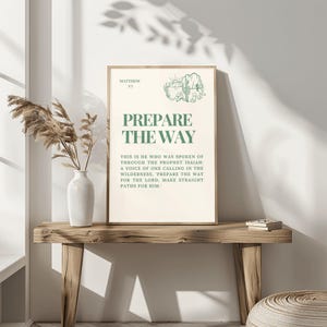 Op de afbeelding: Een beige printbare wandkunstprint met een groene rand en tekst die "Bereid de weg" zegt en een bijbelvers uit Mattheüs 3:3. De tekst luidt: "Dit is hij van wie gesproken is door de profeet Jesaja: Een stem die roept in de woestijn: 'Bereid de weg voor de Heer, maak zijn paden recht.'"