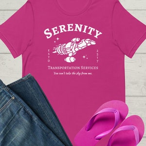 May include: A pink t-shirt with a white graphic of a spaceship with the text "Serenity" above it and "Transportation Services" below it. The text "ESTD 2517" is also included on the graphic. The text "You can't take the sky from me." is printed below the graphic.