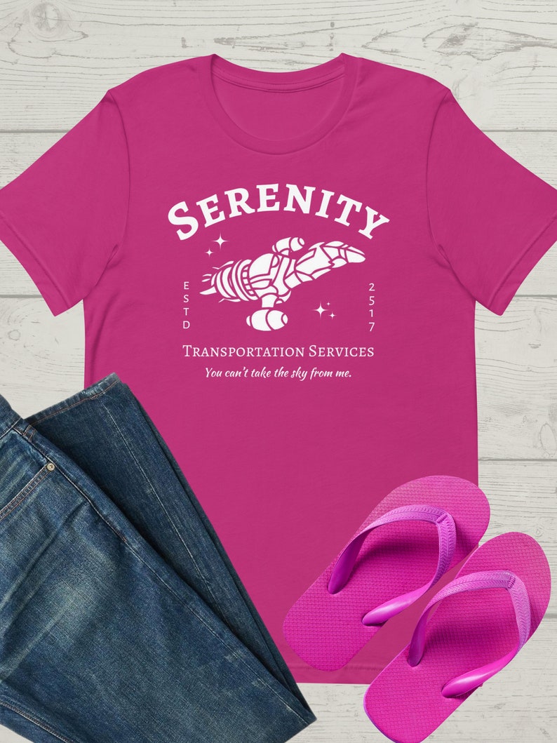 May include: A pink t-shirt with a white graphic of a spaceship with the text "Serenity" above it and "Transportation Services" below it. The text "ESTD 2517" is also included on the graphic. The text "You can't take the sky from me." is printed below the graphic.