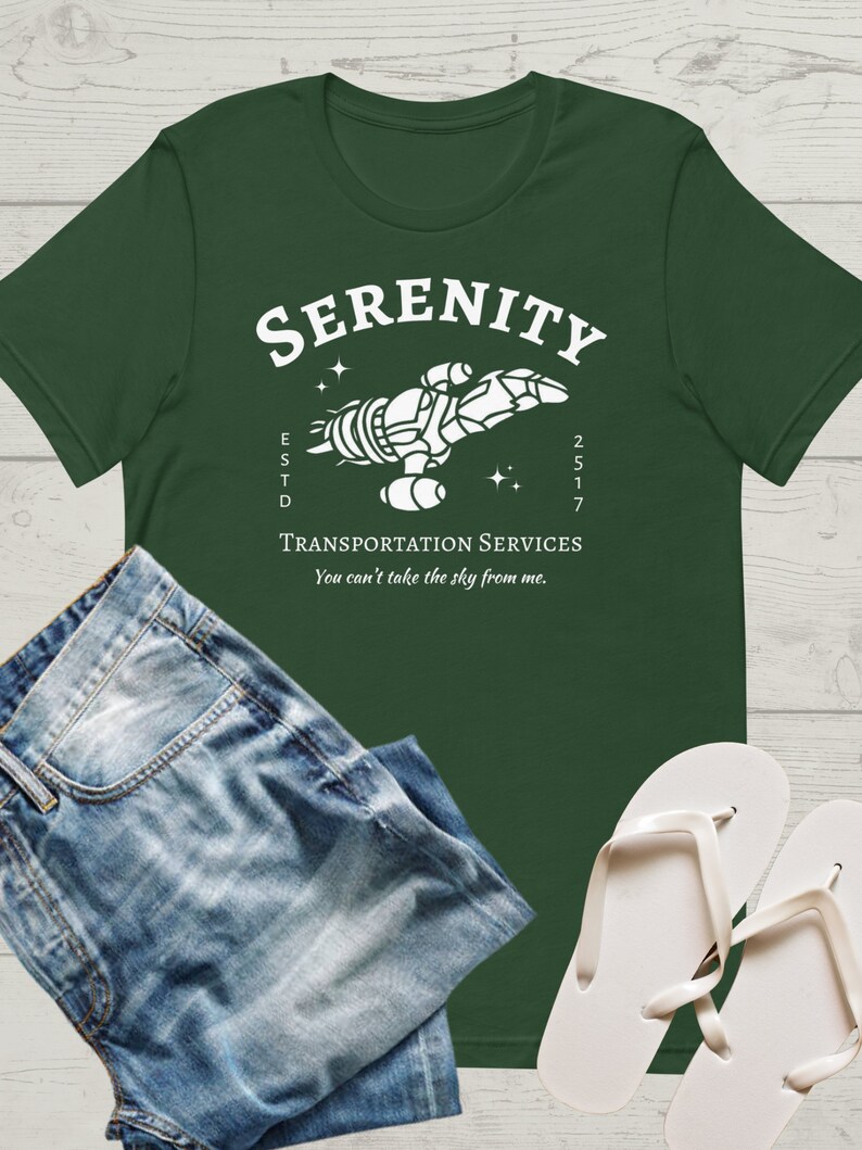 May include: A green t-shirt with a white graphic of a spaceship with the text "Serenity" above it and "Transportation Services" below it. The text "ESTD 2517" is on the left side of the spaceship and the text "You can't take the sky from me." is below the text "Transportation Services".