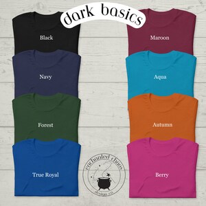 May include: A set of ten folded t-shirts in various colors, including black, maroon, navy, aqua, forest green, true royal blue, and berry. The shirts are arranged in two rows of five, with the text "dark basics" at the top. The text "enchanted chaos design.co." is in a circle at the bottom.