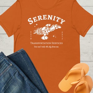 May include: Orange t-shirt with a white graphic of a spaceship with the text "Serenity Transportation Services" and "You can't take the sky from me."